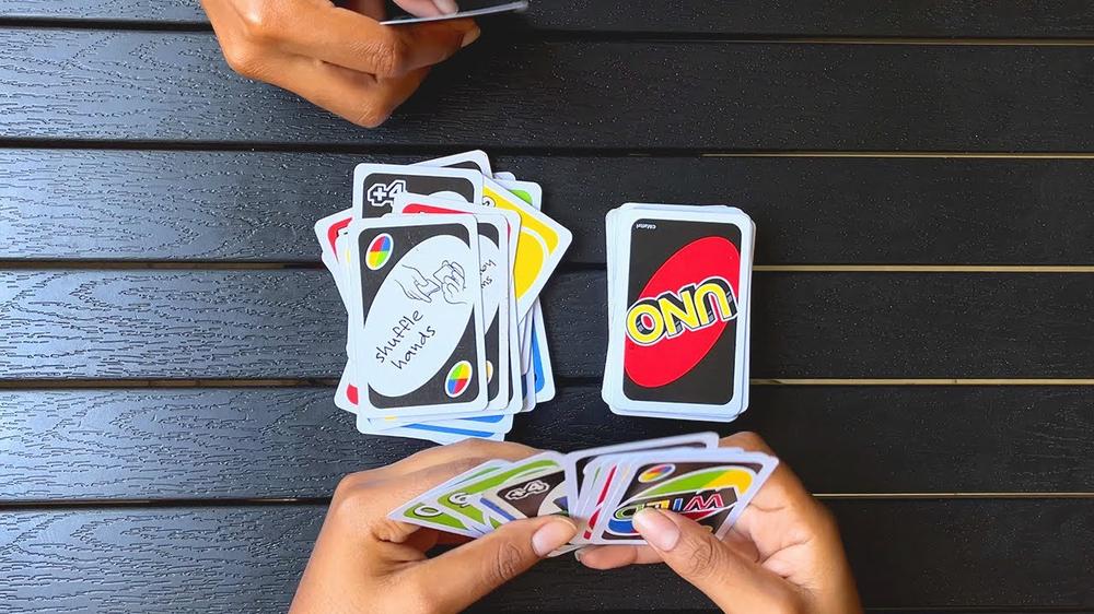 A person is playing the card game Uno with someone else, with a black table as the background.